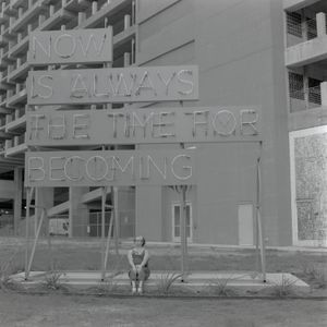 A woman sits beneath a sign neon sign which flips between messages